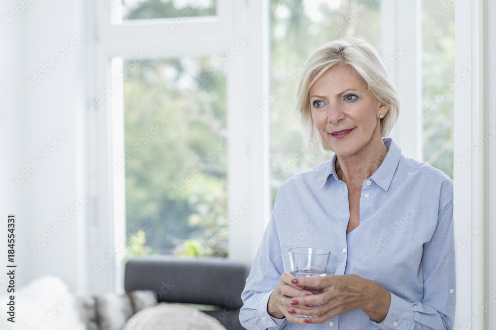 Portrait of smiling senior woman with glass of water in the living room Portrait of smiling senior woman with glass of water in the living room
