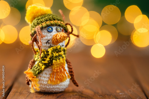 Handmade knitted snowman toy on wooden background with bokeh