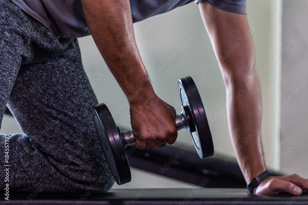 Fototapeta premium Closeup of handsome man doing bodybuilder exercises with dumbbell in ghym
