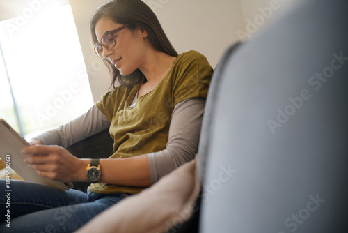 Brunette woman with eyeglasses using tablet, sitting on sofa