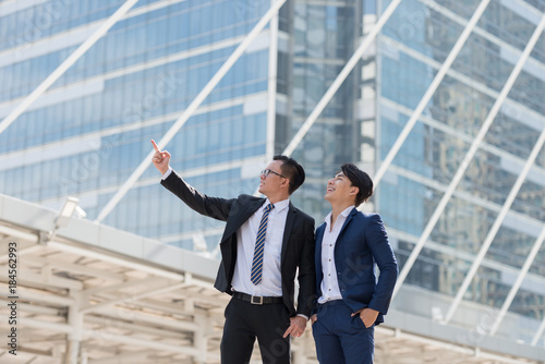 Successful two businessman in suit standing a being pointing finger in city looking go big city buildings, planning new projects, waiting for meeting to start. Copy space for text