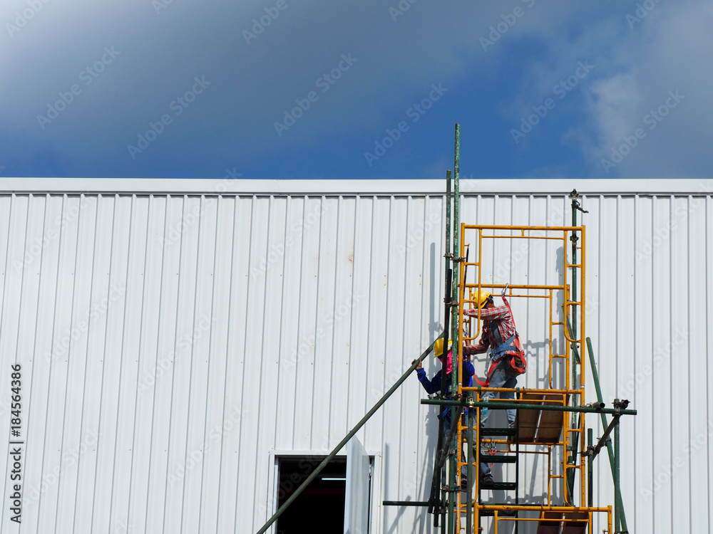 Construction workers working on scaffolding, Man Working on the Working at height with blue sky at construction site Construction workers working on scaffolding, Man Working on the Working at height with blue sky at construction site