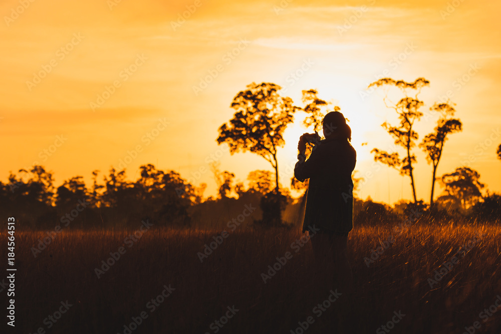 Silhouette of female photographer taking picture of meadow at sunrise Silhouette of female photographer taking picture of meadow at sunrise