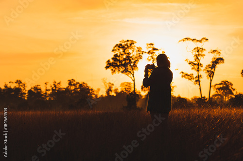Silhouette of female photographer taking picture of meadow at sunrise
