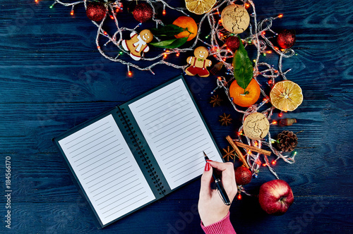 A girl with a red manicure in a knitted pink sweater writes a list of cases for the new year. A list of Christmas presents. Typical festive winter accessories, attributes, ornaments. photo