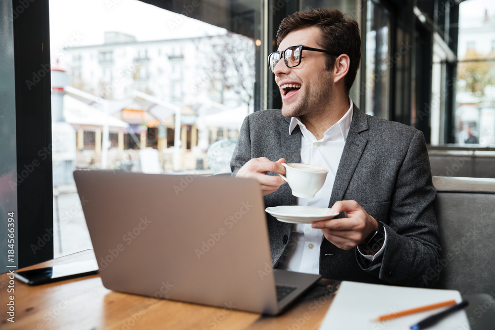 Fototapeta premium Laughing business man in eyeglasses sitting by table in cafe
