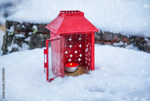 Red lantern with burning candle on fresh snow. Snowy winter morning in park.
