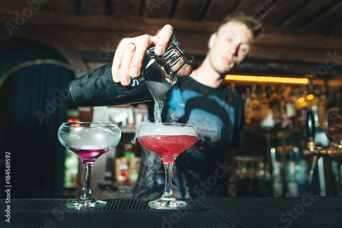 A barman pours mixed alcohol from a shaker into a glass. Creation of beautiful alcoholic cocktails at the bar.