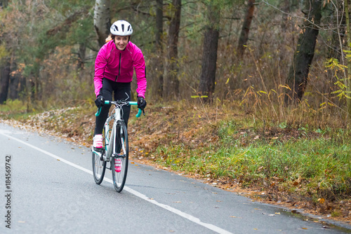 Young Woman in Pink Jacket Riding Road Bicycle in the Park in the Cold Autumn Day. Healthy Lifestyle. © Maksym Protsenko