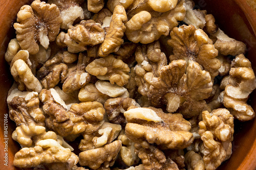a lot of natural walnuts in a brown ceramic bowl on a white background