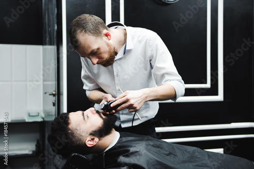 Master cuts hair and beard of men in the barbershop, hairdresser makes hairstyle for a young man