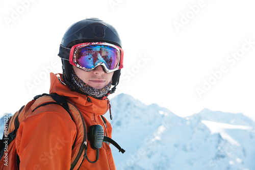 Portrait of a skier in an orange overall with a backpack on his back in a helmet stands against the background of a beautiful Caucasian mountain landscape © yanik88