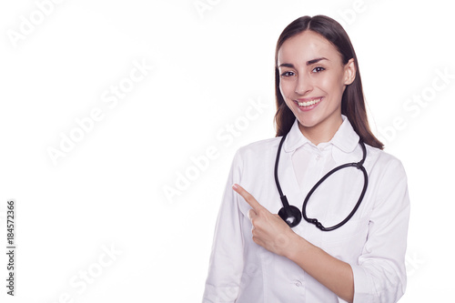 Smiling attractive modern doctor with stethoscope isolated on white background and pointing on copyspace