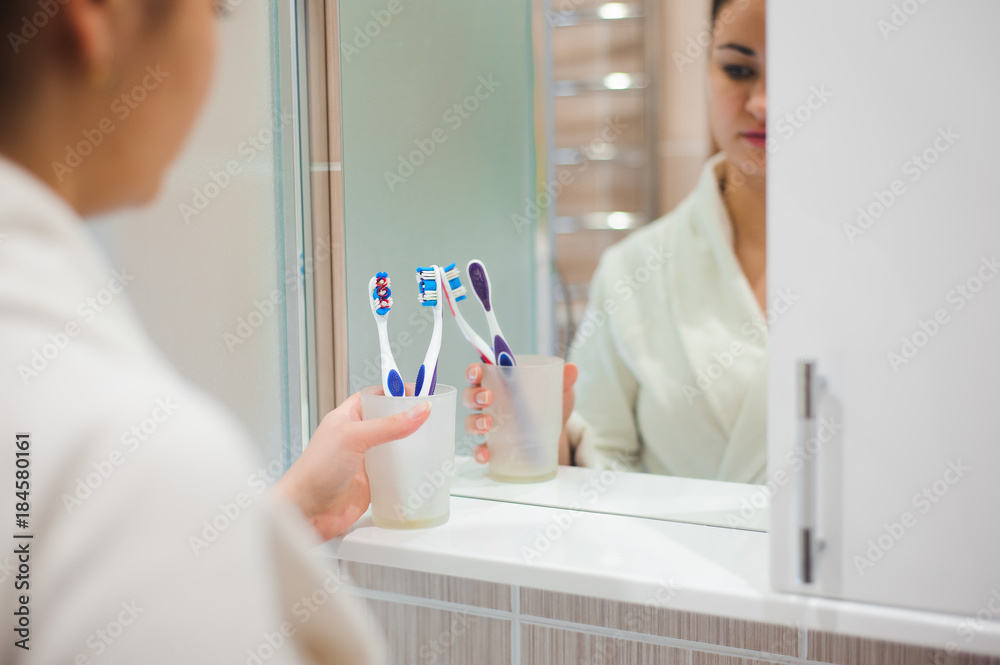 Fototapeta premium Image of pretty female brushing her teeth in front of mirror in the morning
