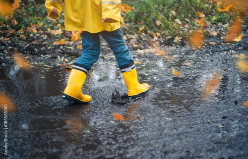 Child with Yellow Rain Boots Playing outdoors in an Autumn Forest jumping in puddles enjoying nature with Falling Leaves