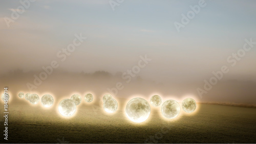 Surreal, mysterious photo collage of glowing moons hover over a foggy farmer's field. photo