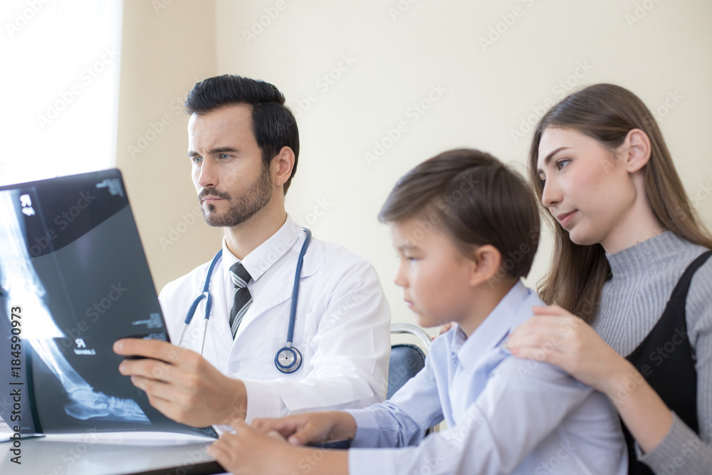 Portrait of People and doctor looking to x-ray film with serious emotion. Doctor showing x-ray film to boy and woman at hospital. People with medical concept. Portrait of People and doctor looking to x-ray film with serious emotion. Doctor showing x-ray film to boy and woman at hospital. People with medical concept.