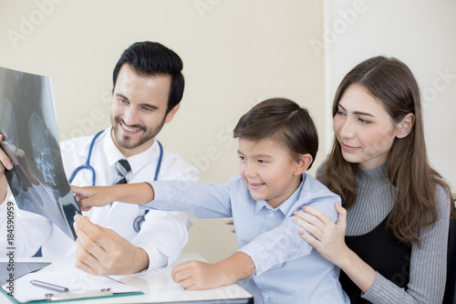 Portrait of smiling handsome doctor working in hospital. Doctor showing x-ray film to boy and woman with happy emotion.
