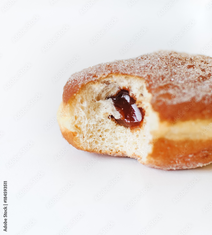 German fried donut, so called Krapfen, Berliner or Pfannkuchen, filled with rose hip jam and dusted with cinnamon sugar, traditionally eaten at carnival and at New Year's Eve on white background German fried donut, so called Krapfen, Berliner or Pfannkuchen, filled with rose hip jam and dusted with cinnamon sugar, traditionally eaten at carnival and at New Year's Eve on white background
