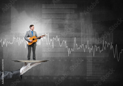 Businessman on metal tray playing acoustic guitar against graphs background