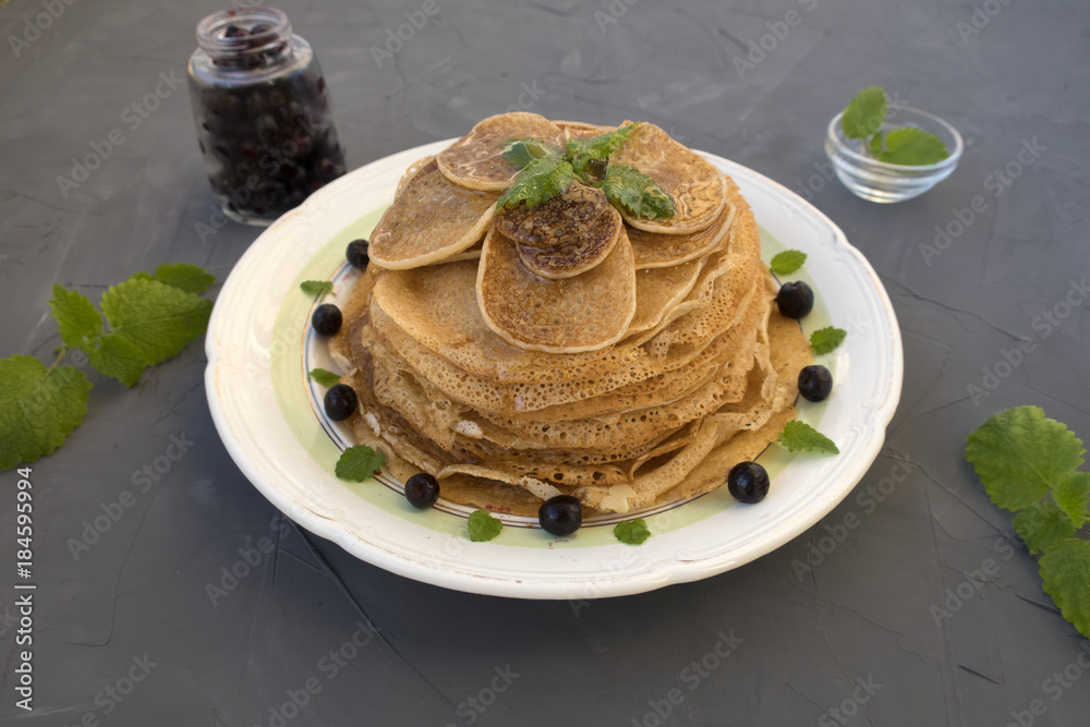 Pancakes are located in a plate on a gray background, decorated with berries and mint leaves. Pancakes are located in a plate on a gray background, decorated with berries and mint leaves.