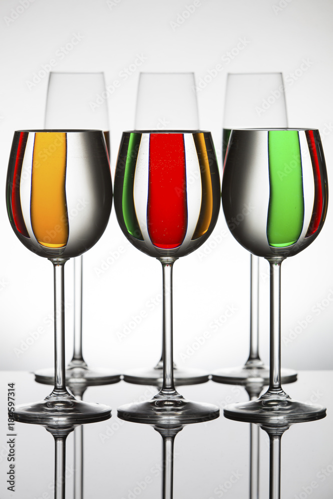 Wineglasses on a shiny surface with different colour fluids that distort reflection Wineglasses on a shiny surface with different colour fluids that distort reflection