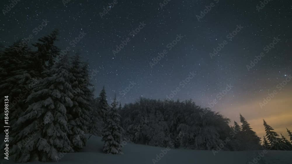Christmas winter night landscape with stars sky moving over snowy trees. Astronomy time lapse zoom in