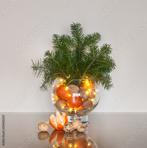 Decorative Christmas arrangement with fir branches, oranges and walnuts in the glass vase 