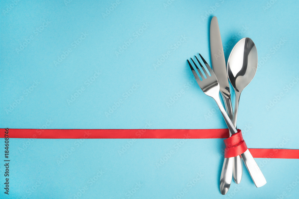 Fork, spoon and knife tied with a red ribbon on blue background