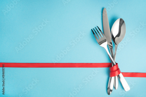 Obraz na płótnie Fork, spoon and knife tied with a red ribbon on blue background w salonie