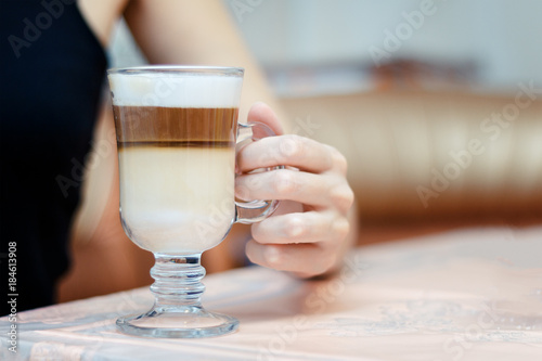 The girl sitting at the table inderjit a glass of latte.