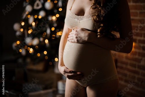 Pregnant belly of long-haired woman standing against Christmas tree