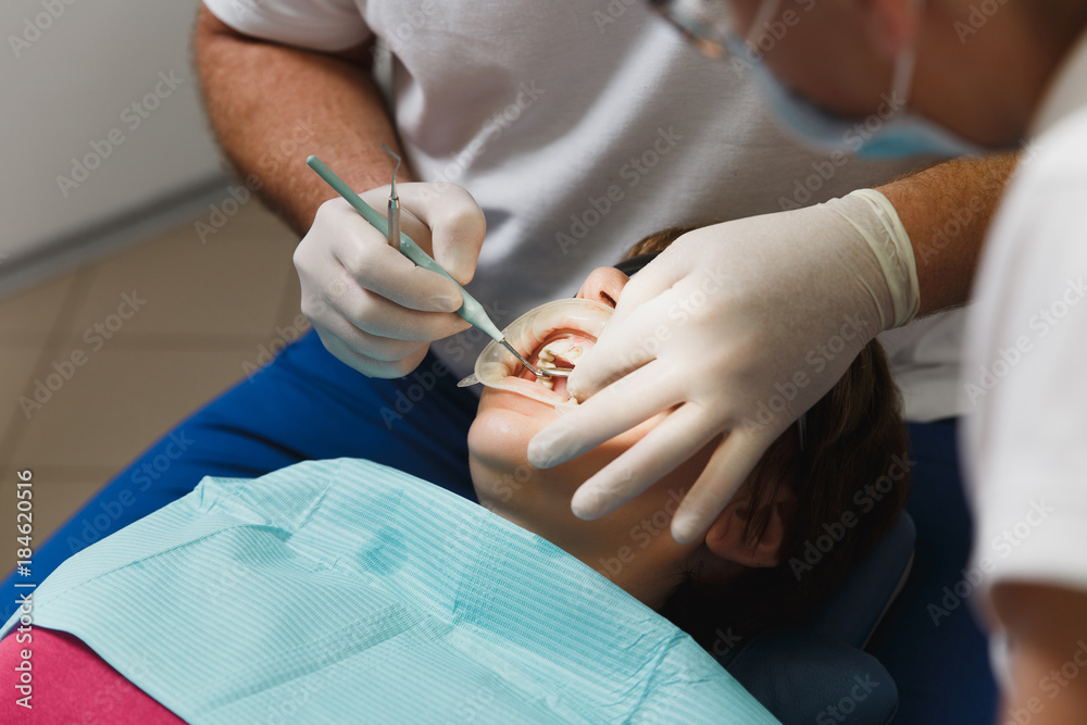 Close up process of preparing and installing dental ceramic crown. Male professional dentist helps to treat the teeth of woman patient in clinic light office with modern tools equipment. Open mouth.