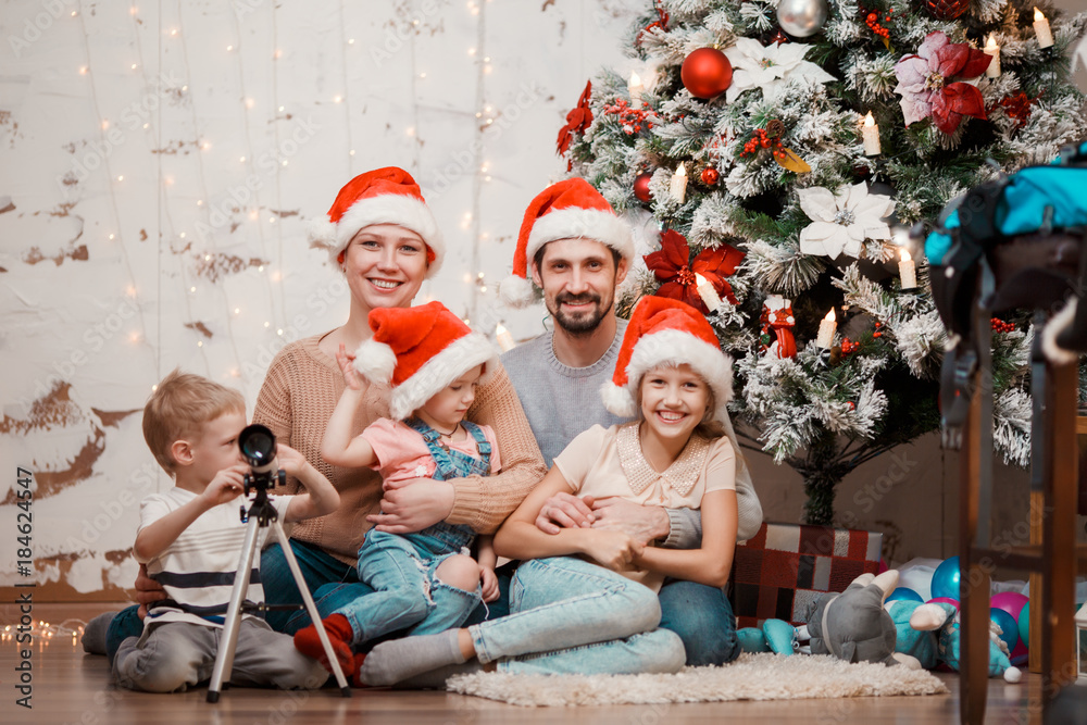 Image of parents, two daughters in caps of Santa and son with telescope Image of parents, two daughters in caps of Santa and son with telescope