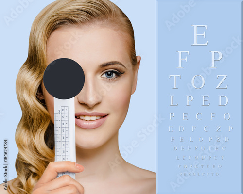 Face smiling woman, checking vision, closing eye with special tool, holographic eye chart on the background. The vision test concept