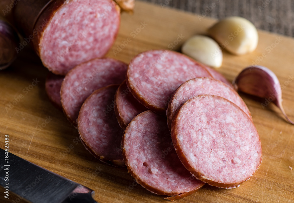 Slices of sausage and garlic lie cutting board Slices of sausage and garlic lie cutting board