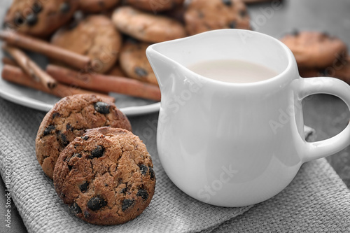 Chocolate chip oatmeal cookies and jug of milk on table, closeup