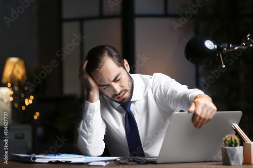 Vászonkép Tired young man using laptop in office at night