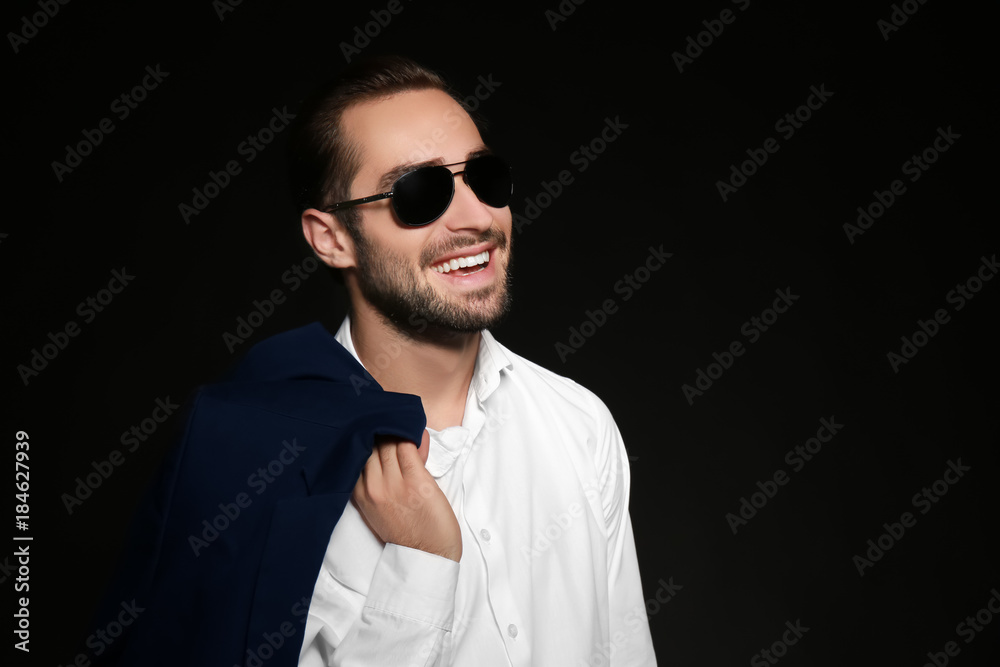 Obraz premium Young handsome man in sunglasses smiling on black background