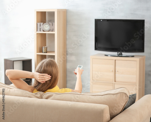 Beautiful woman watching TV while resting on sofa at home