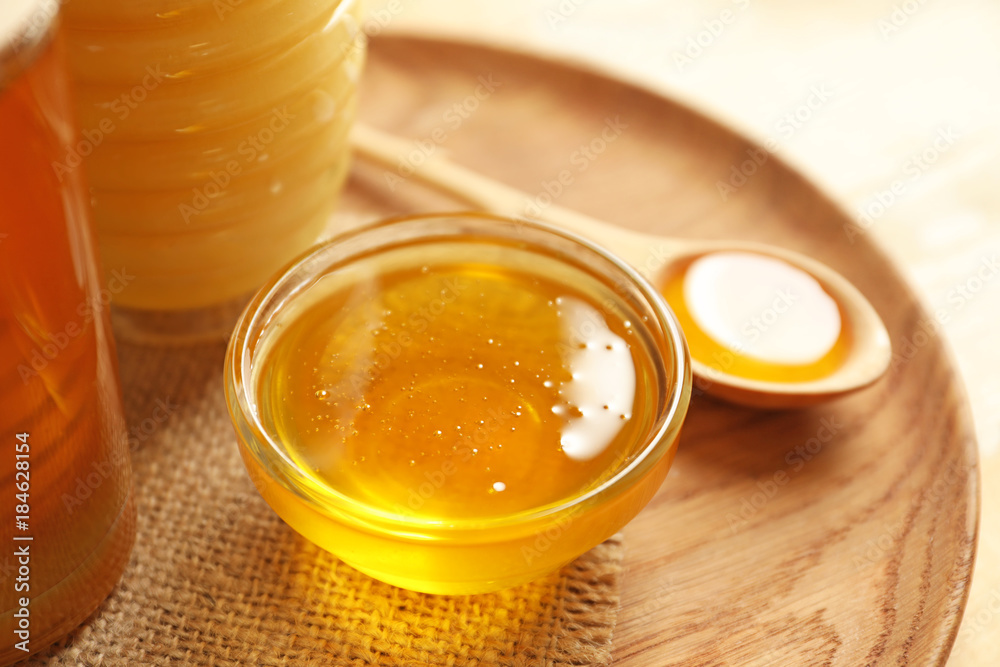 Glass bowl with honey on wooden plate, closeup Glass bowl with honey on wooden plate, closeup