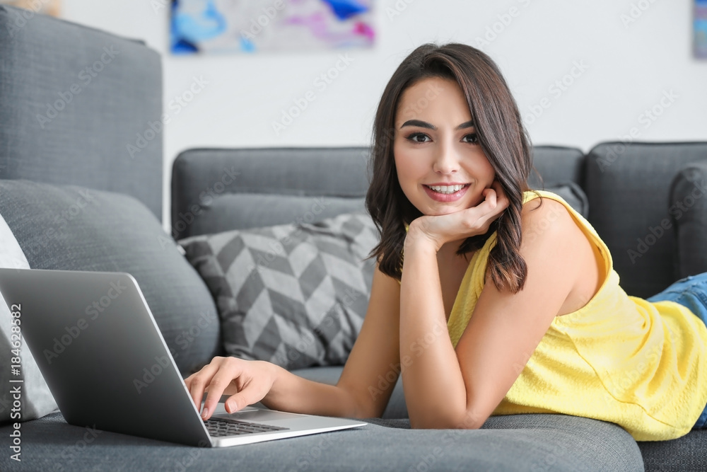 Young woman with laptop lying on sofa at home Young woman with laptop lying on sofa at home