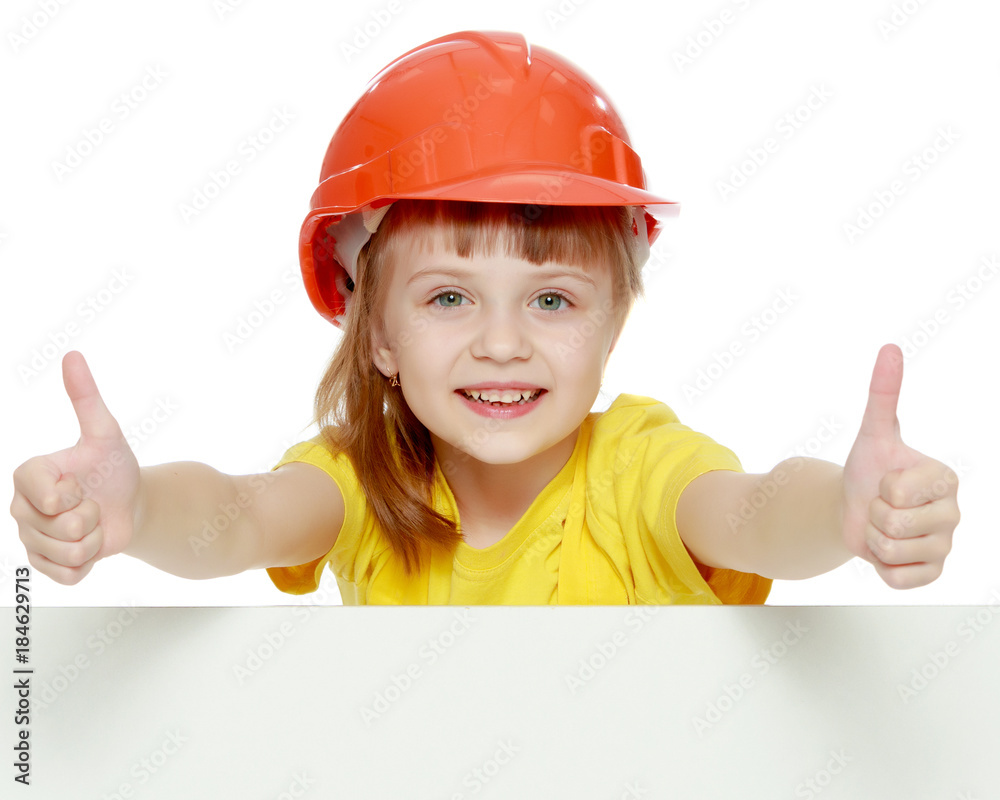 Girl in a construction helmet peeks out from behind a billboard. Girl in a construction helmet peeks out from behind a billboard.