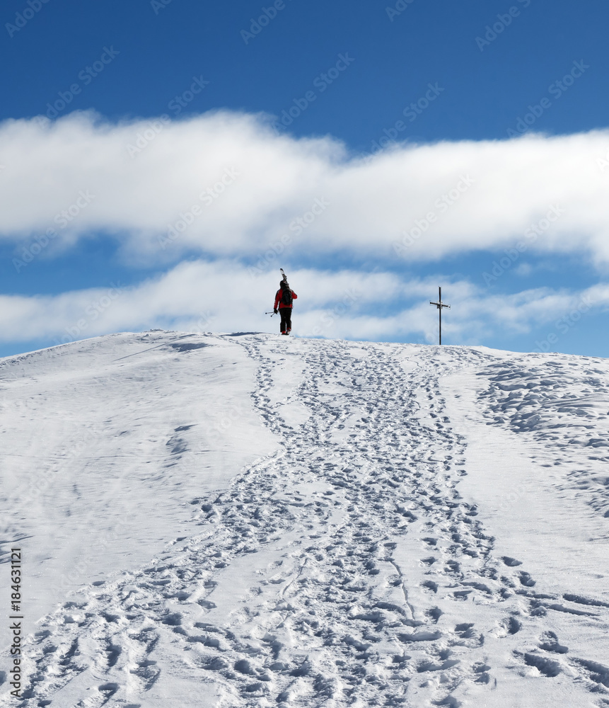 Skier with skis on his shoulder go up to top of snowy mountain