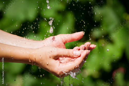 Woman washing hand outdoors. Natural drinking water in the palm. Young hands with water splash  selective focus