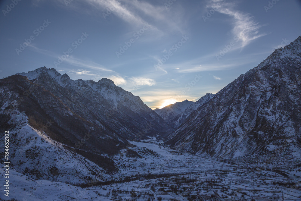 Вечерний пейзаж, оранжевые облака в небе над снежными горными склонами, природа Северного Кавказа