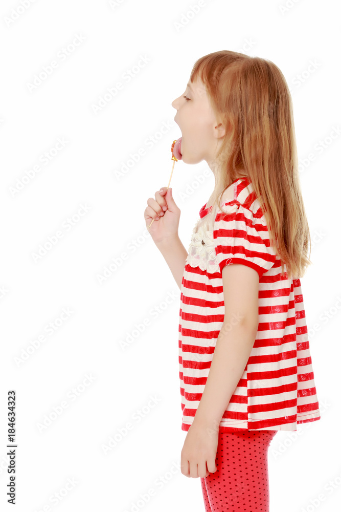 A little girl licks a candy on a stick.
