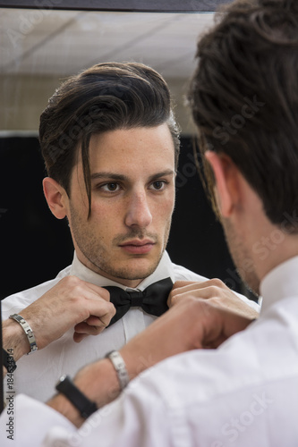 Mirror reflection of elegant handsome man wearing bow-tie and looking at himself