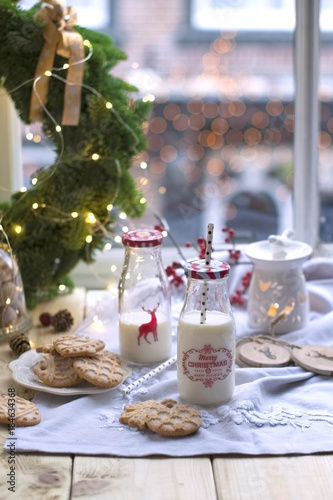 girl milk in a glass at the table by the window  cookies on a plate  and a wreath of Christmas tree