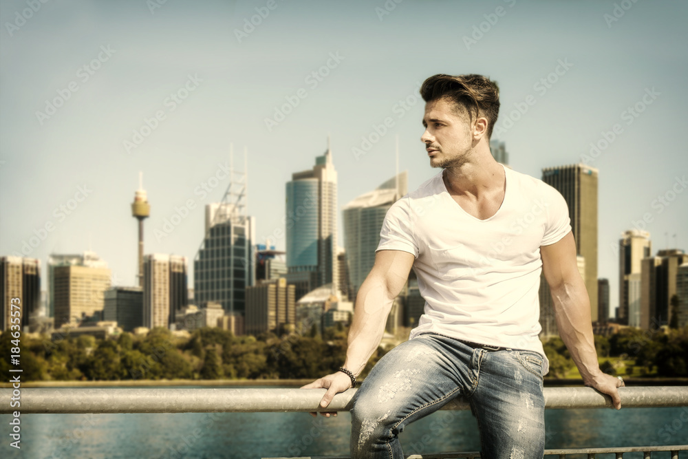 Handsome man sitting on handrail on the background of city skyline. 